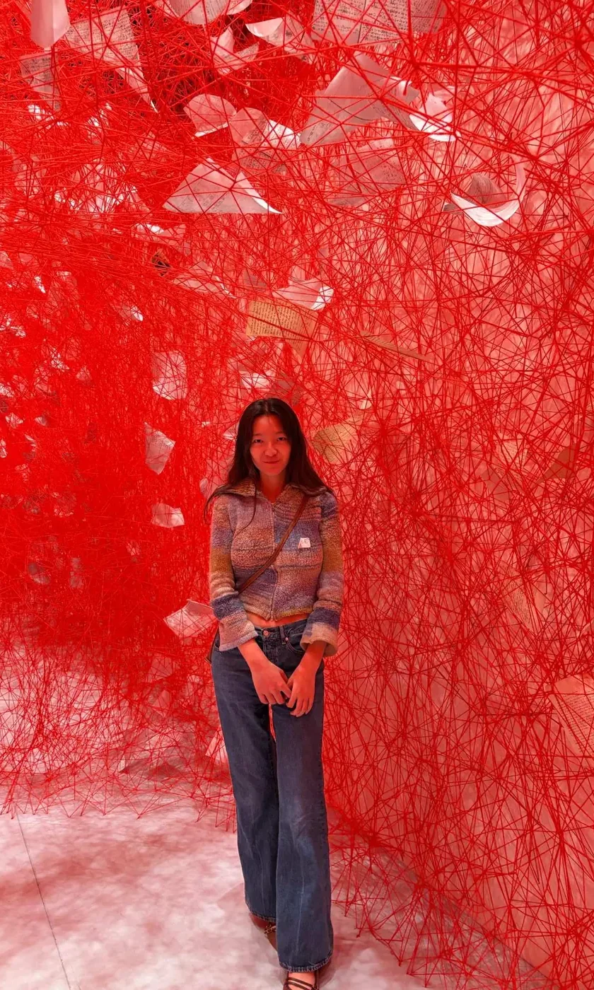 Muyi standing inside a room-filling installation of red thread and paper